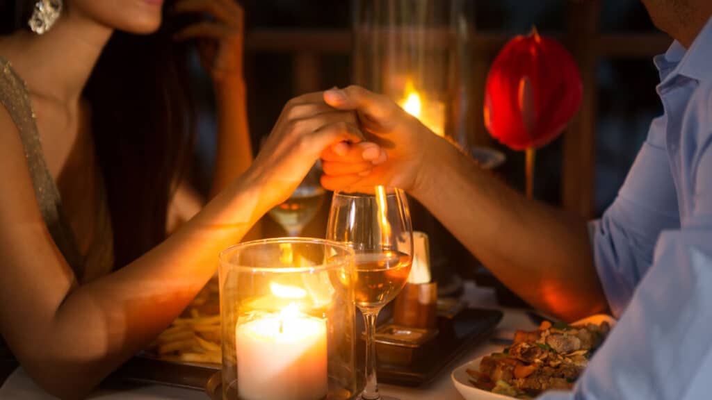 Romantic couple holding hands together over candlelight during romantic dinner