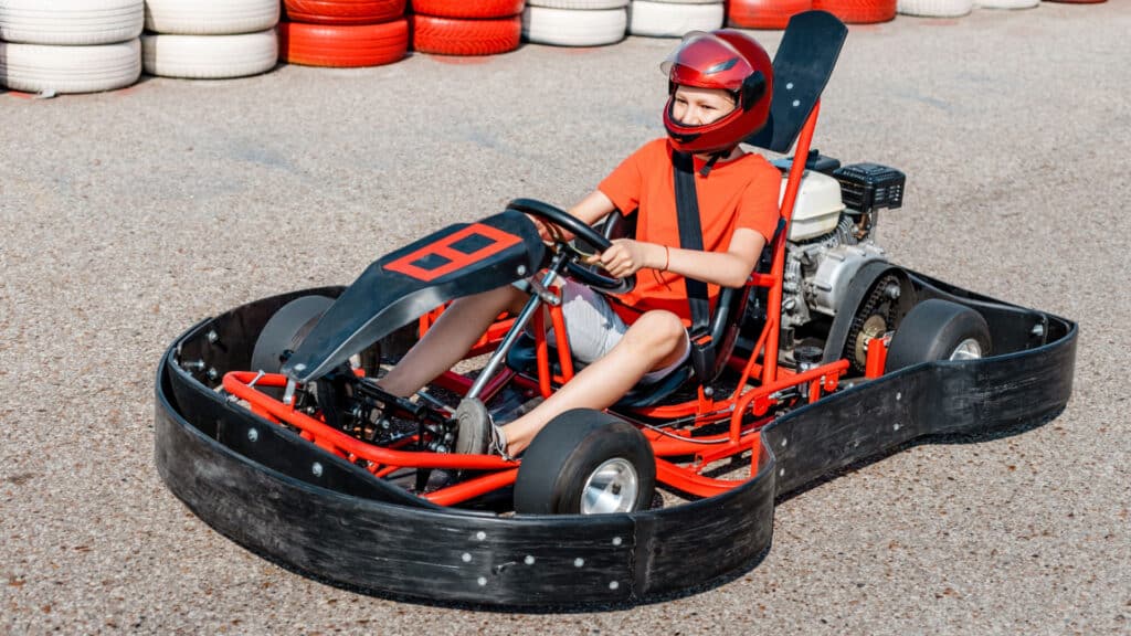 Happy teenage boy driving a go-kart car cuts circles around the cartodrome. Hobbies and extreme sports for a child and the fulfillment of a dream
